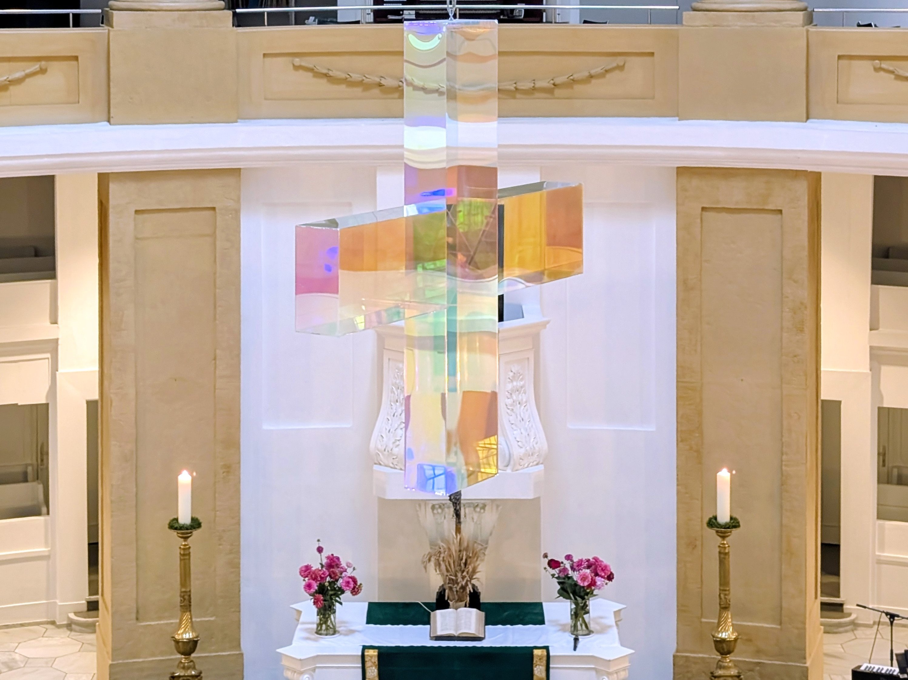 Altarraum der St.-Lamberti-Kirche in Oldenburg mit einem farbig schimmernden Kreuz, zwei brennenden Kerzen, Blumen und der großen Orgel im Hintergrund.