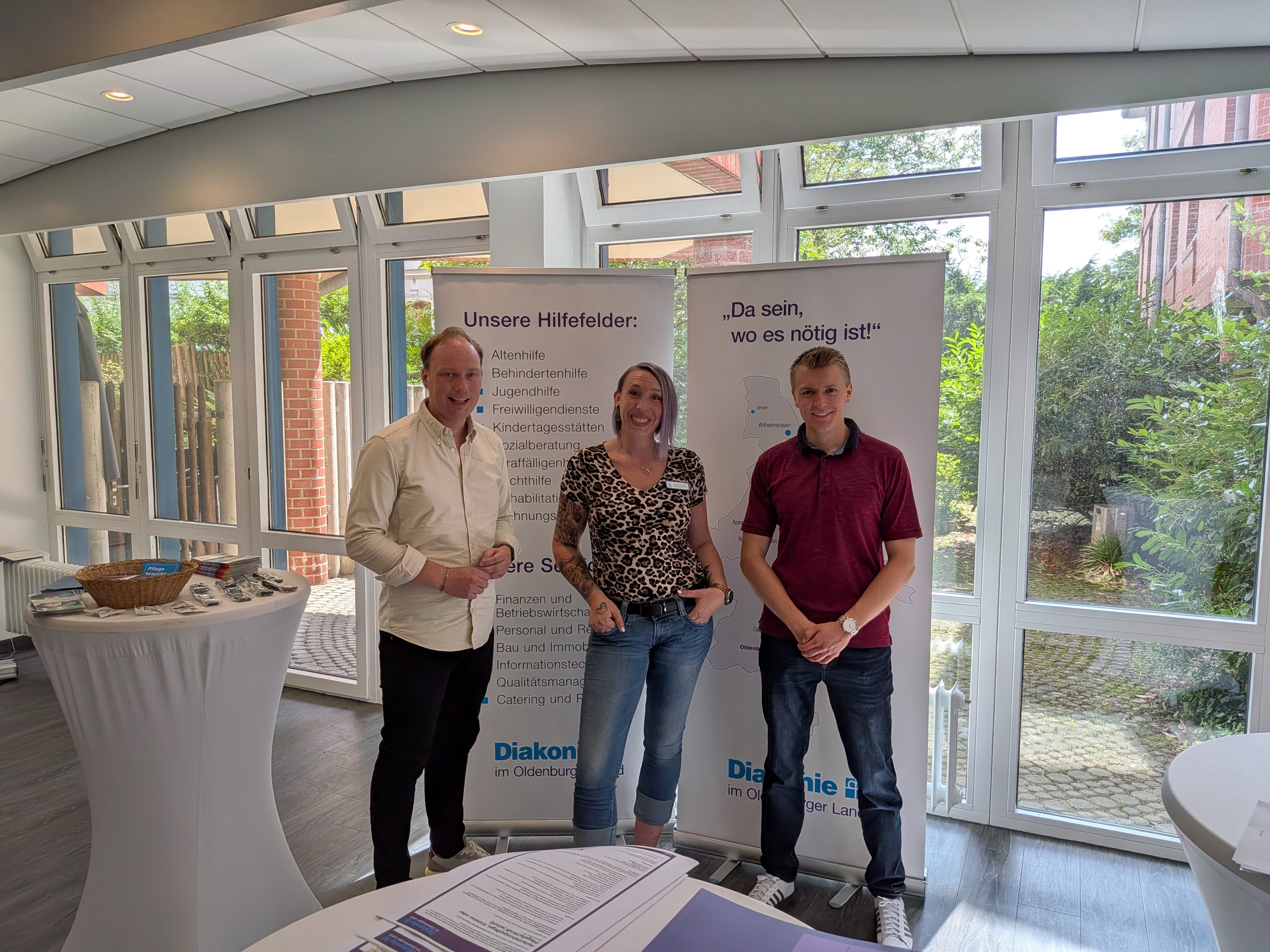 Nils Halm, Jacqueline Beyer und Justin Hoop stehen vor zwei Roll-up-Bannern der Diakonie im Oldenburger Land und präsentieren die Organisation bei den Bewerbertagen im St. Bernhard Hospital in Brake.