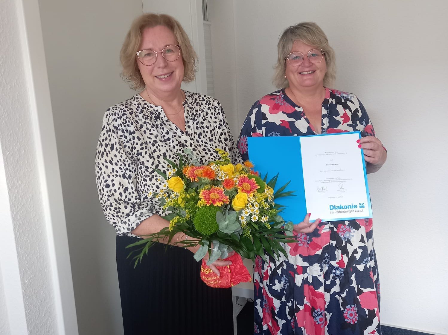 Geschäftsführerin Martina Fisser gratuliert Liane Tappe zum 15-jähriges Dienstjubiläum im Diakoniebüro Vechta und überreicht ihre eine Urkunde und einen Blumenstrauß. 