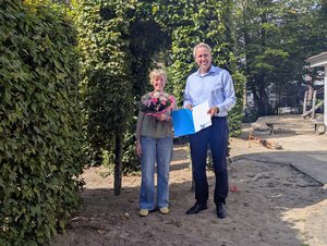 Einrichtungsleiterin Astrid Brundiers steht mit einem Blumenstrauß neben dem Kaufmännischen Vorstand Mario Behrends, der ihr zum 35-jährigen Dienstjubiläum eine Urkunde überreicht.